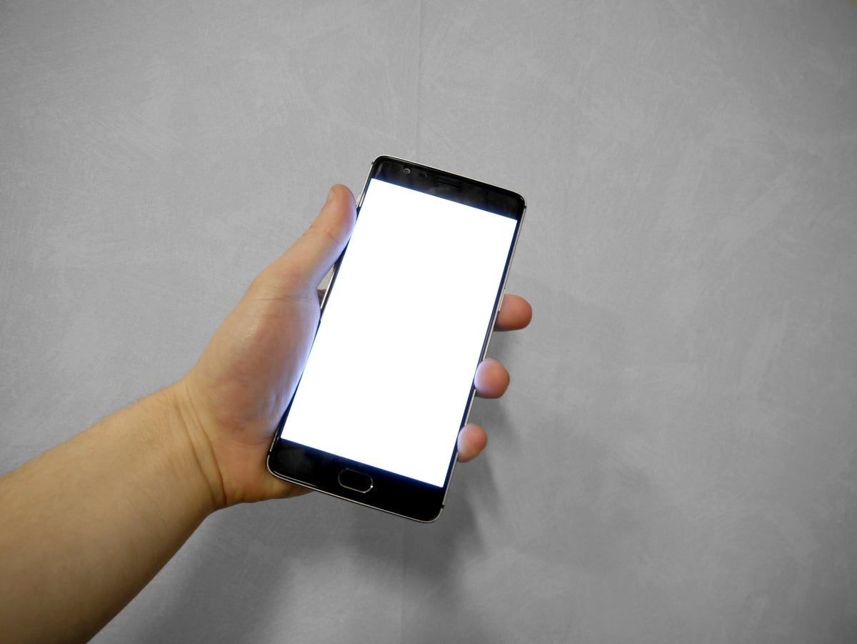 Hand die een smartphone met helder wit scherm vasthoudt in het donker